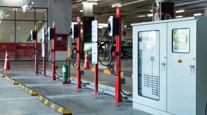 A row of red electric vehicle charging stations with cables and safety cones, set up in a parking garage.