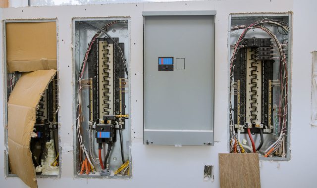 An open electrical panel with multiple circuit breakers and neatly organized wiring, set within a wall.