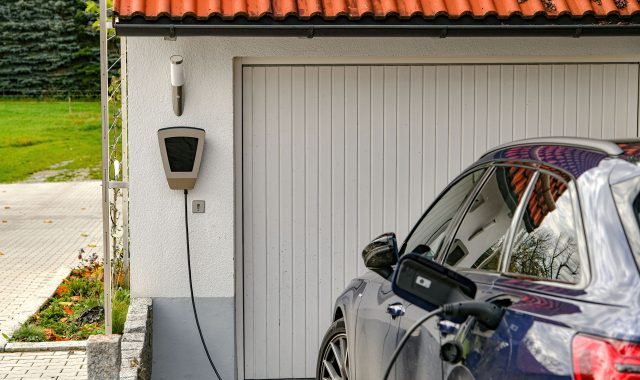 An electric vehicle plugged into a wall-mounted charger outside a home, demonstrating home-based EV charging solutions.
