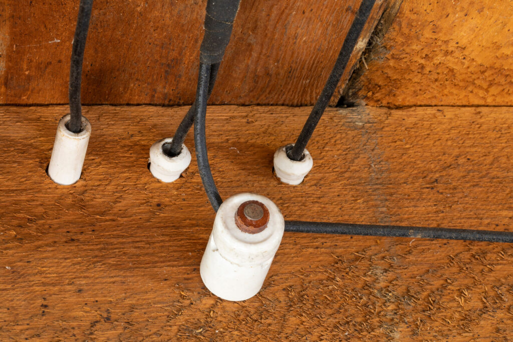Old-fashioned knob-and-tube wiring secured with ceramic insulators, showcasing traditional electrical installation methods.