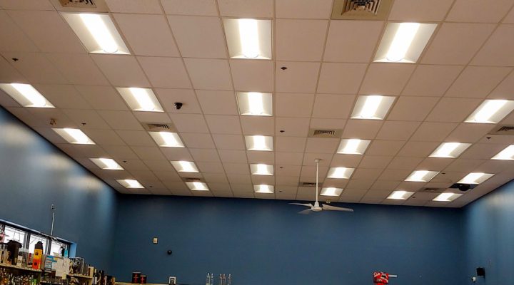 A retail space with a ceiling featuring evenly spaced fluorescent lights and ceiling fans for ventilation.