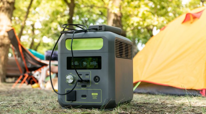 A rugged portable power station with multiple outlets and USB ports, set up outdoors near a tent and camping gear.
